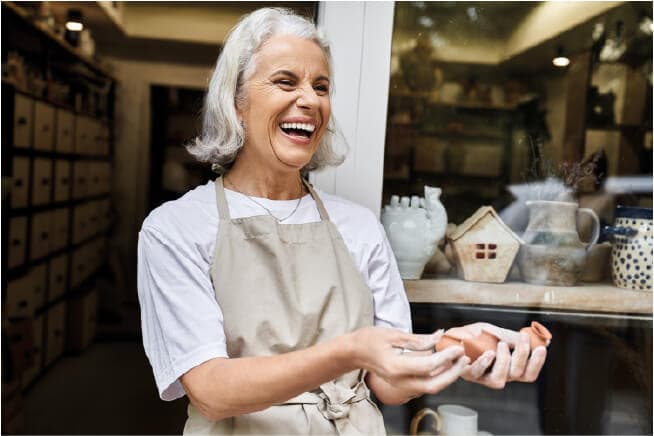 Artigiana sorridente mostra un manufatto in ceramica davanti al suo laboratorio
