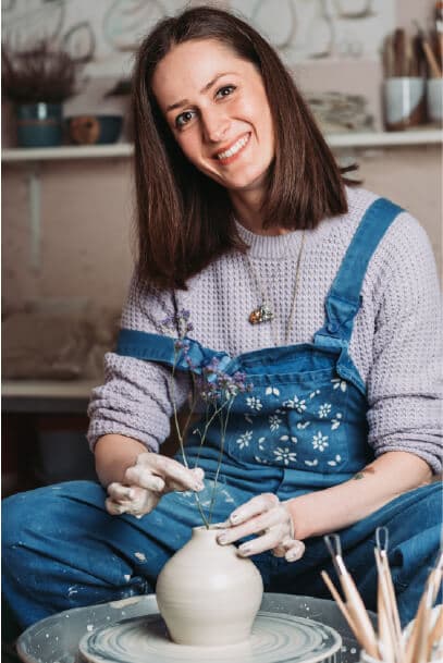 Artigiana sorridente mostra un manufatto in ceramica davanti al suo laboratorio